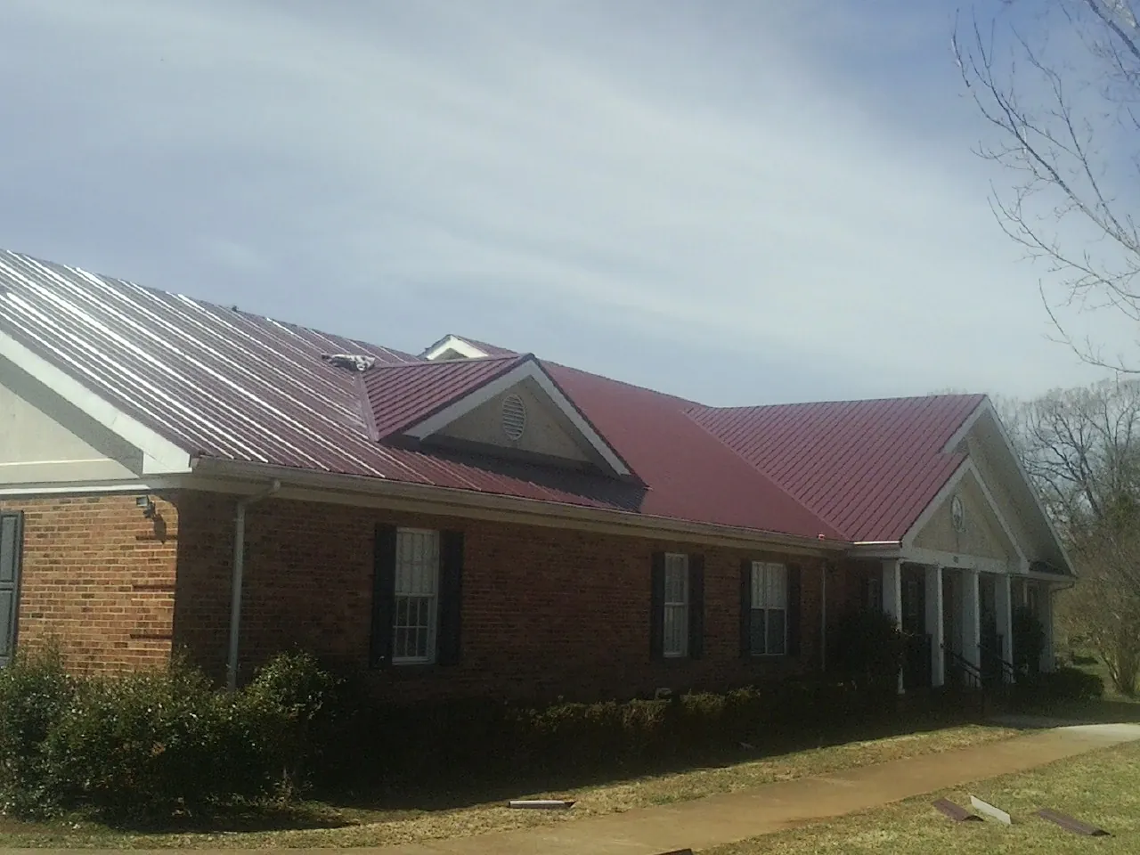 Red metal roof with gabled entries on a long brick building, from a Hail Damage Roof Repair job in Seabeck