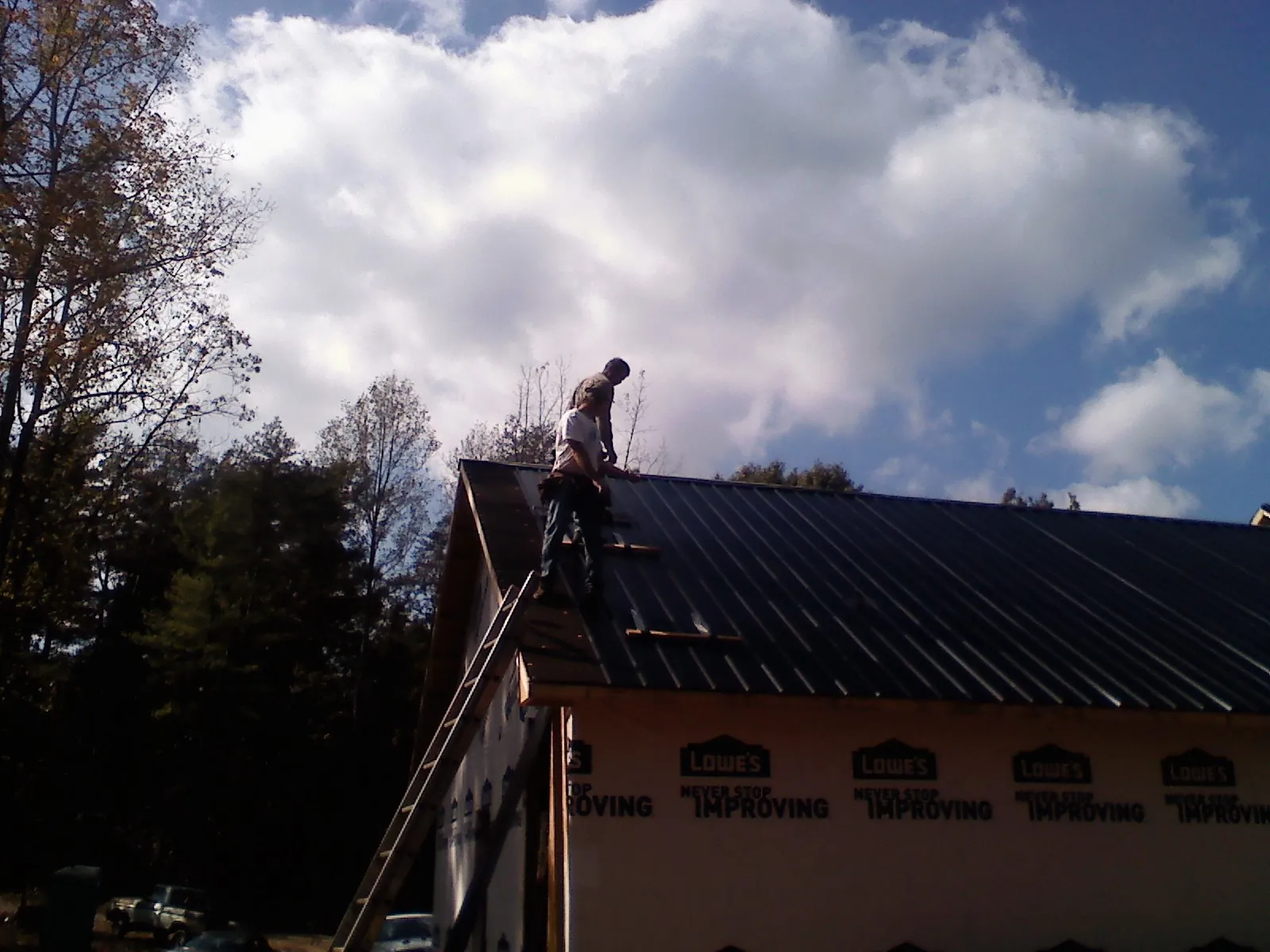 Roofer fastening dark metal panels high against a cloudy sky, from a Roof Inspection job in Seabeck