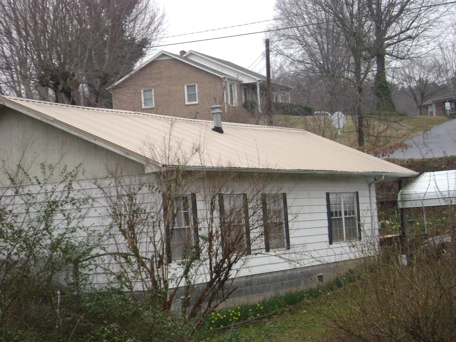 Tan metal roof on a white sided house set into a hillside — Commercial Roofing by Roofing Brothers in Seabeck